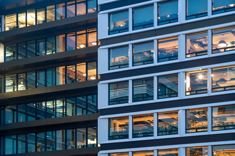 Two buildings with large windows and the lights on