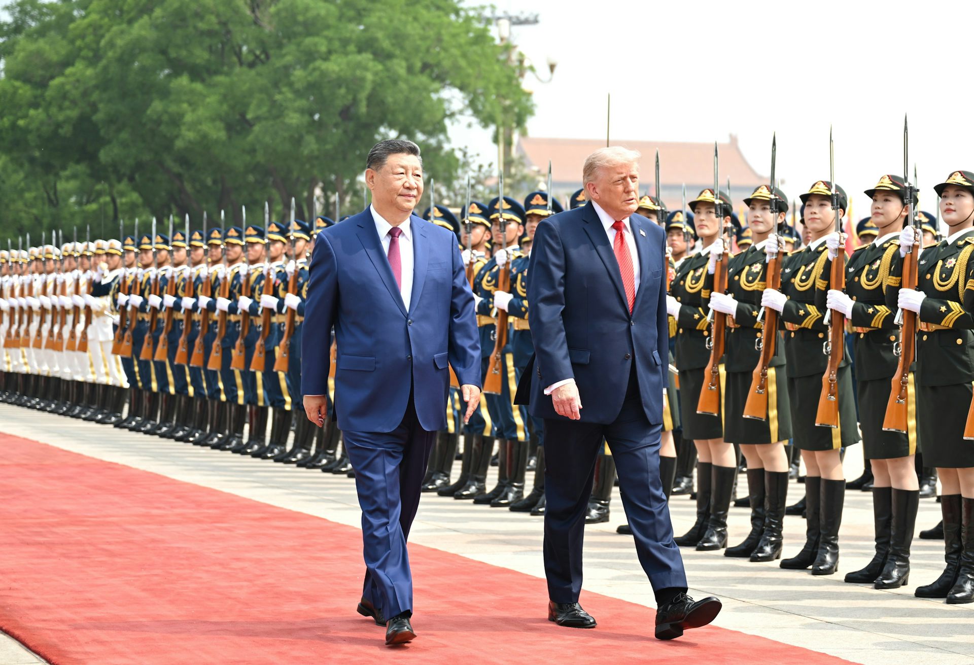 Two men in suits walk past a line of military dressed people.