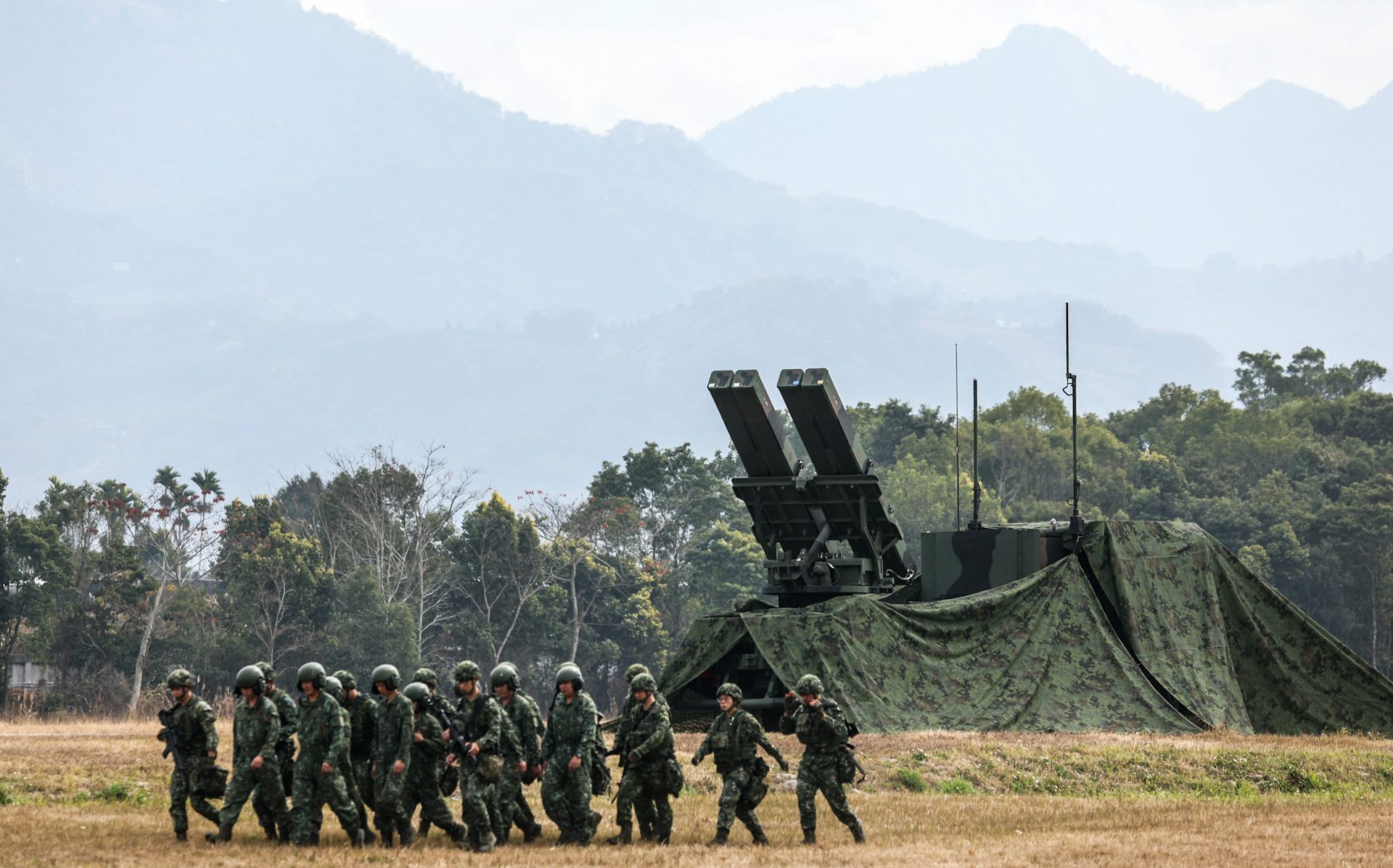 Un grupo de hombres con uniformes militares pasa junto a un gran lanzacohetes.