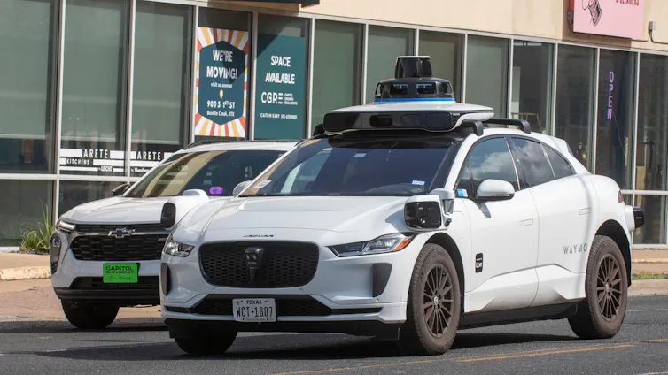 Two Waymo taxis in a Texas street.