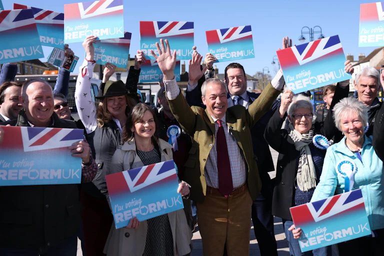 reform uk leader nigel farage with his arms in the air surrounded by supporters waving placards