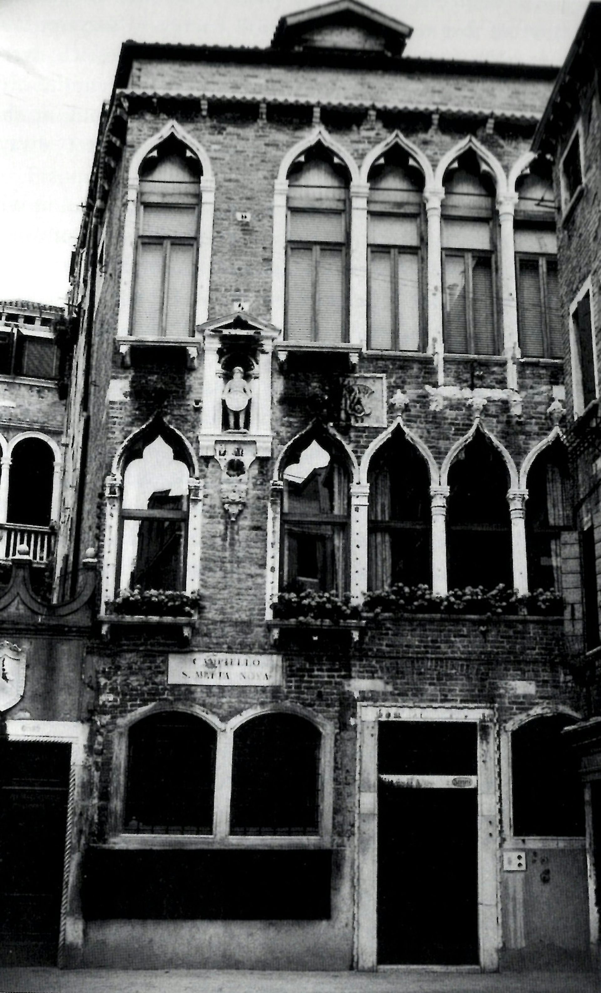 Fotografía en blanco y negro de un antiguo edificio de tres pisos con ventanas altas y delgadas.