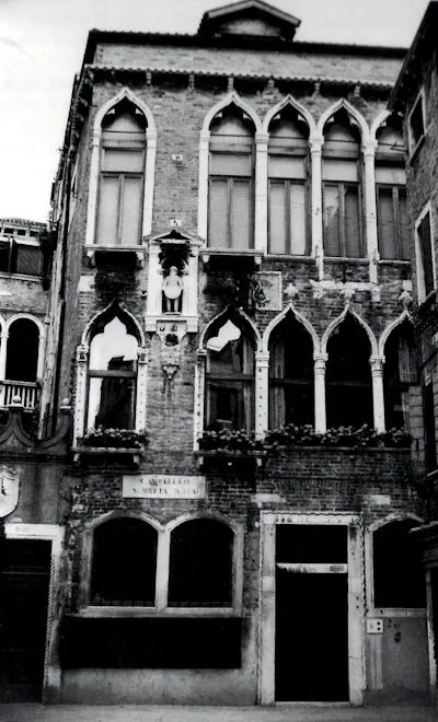 A black-and-white photo of an old, three-story residence with thin, tall windows.
