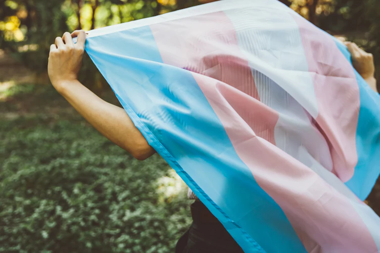 Close-up of large trans flag a person has draped over their back outside