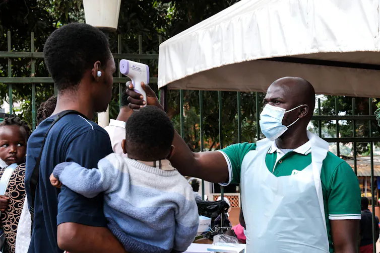 A health official uses a thermometer to screen people in front of Kibuli Muslim Hospital in Kampala, Uganda, May 16 2026.