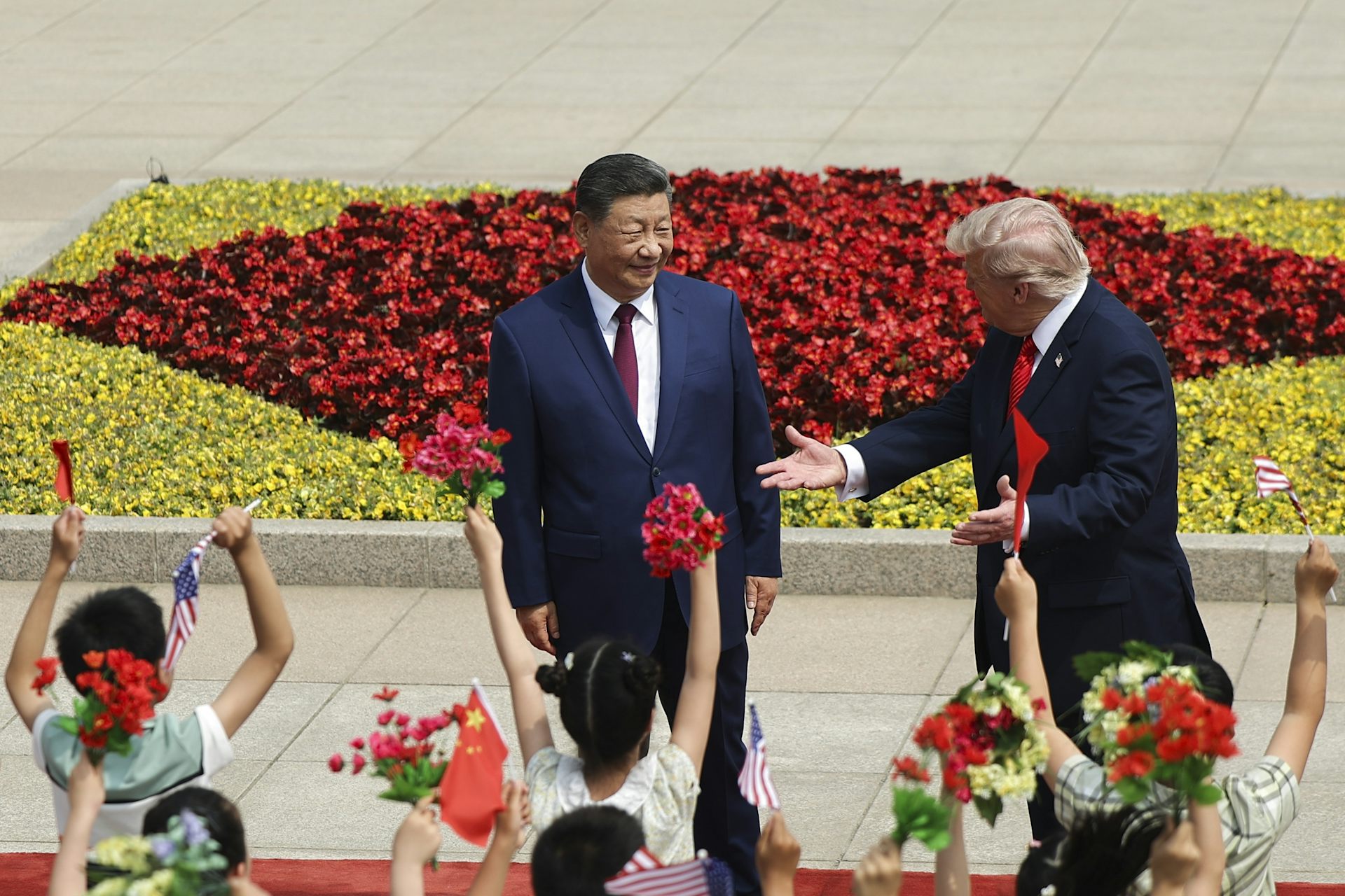 Donald Trump getures towards XI Jinping with dancing Chinese girls in costume in the foreground.