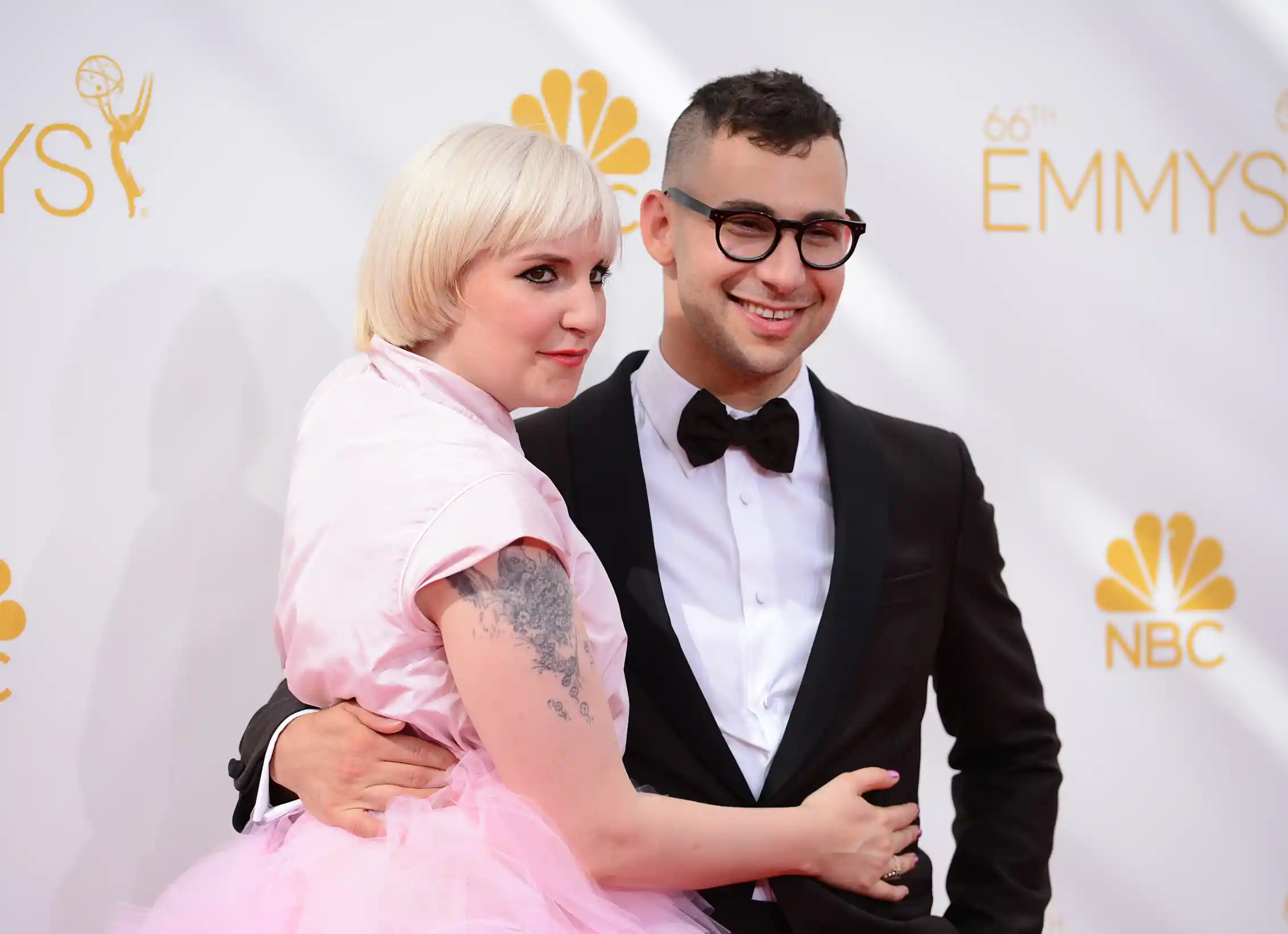 a woman with shot white-blonde hair in a pink dress, with a man in a tuxedo and black glasses, with a small mohawk