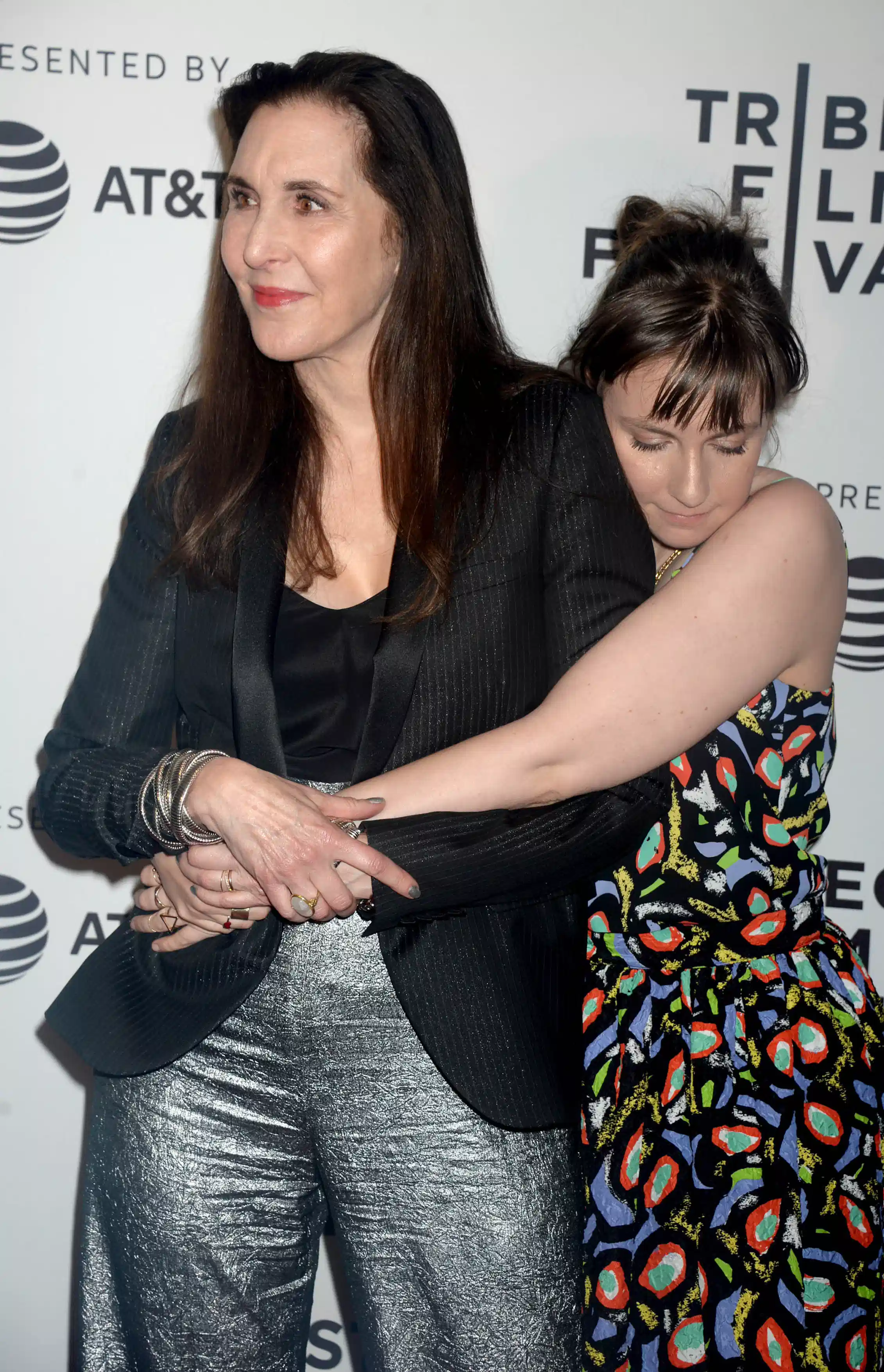 a young woman in a floral dress hugging her well dressed mother from behind, eyes close
