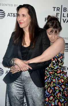 a young woman in a floral dress hugging her well dressed mother from behind, eyes close