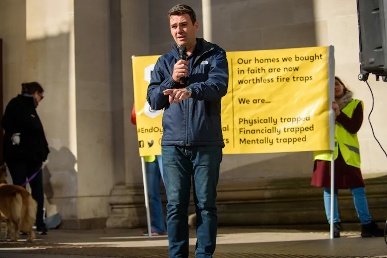 andy burnham holding a microphone and addressing an audience.