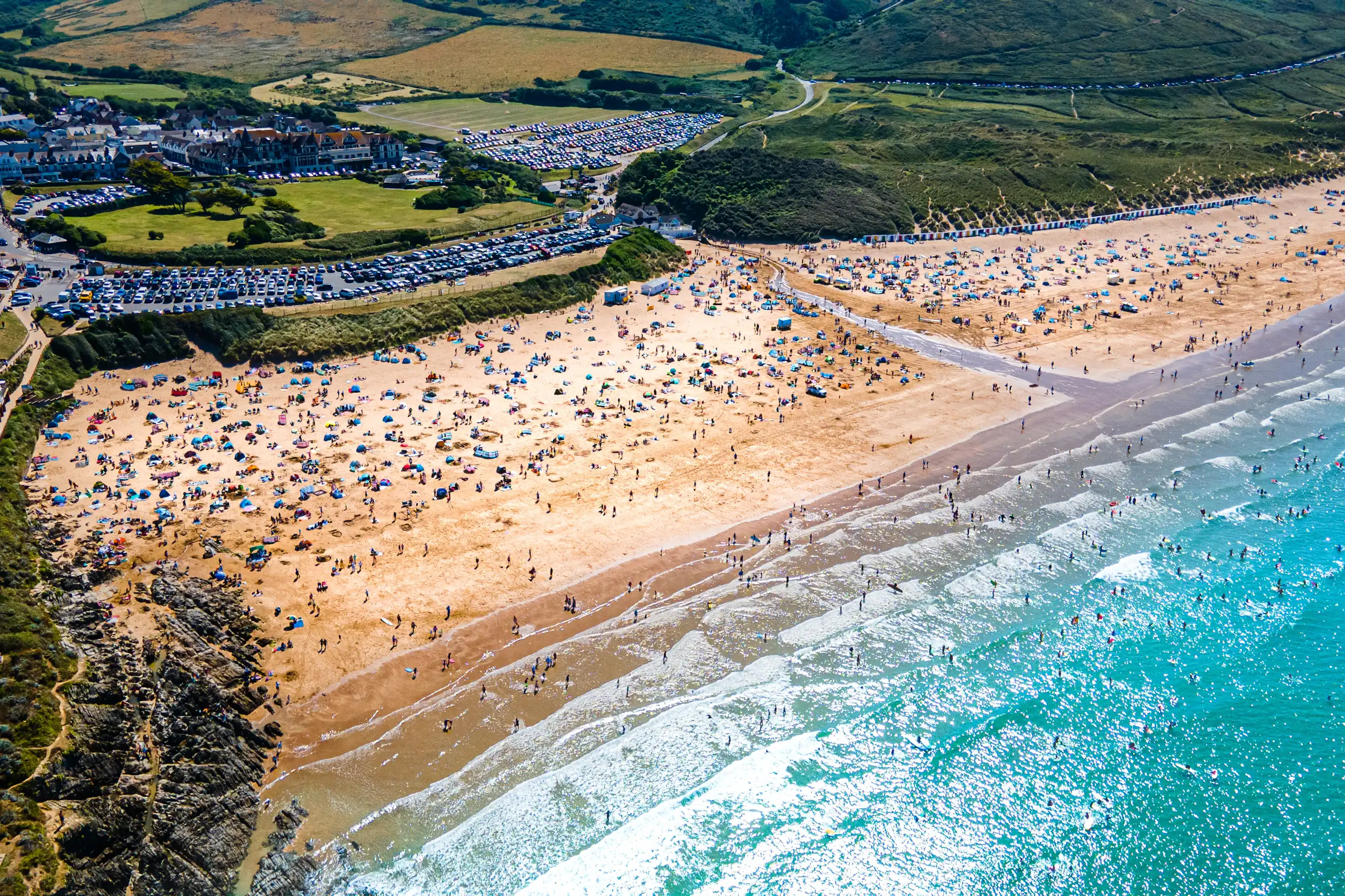 aerial shot of very busy beach, blue seas, hilly green coastline