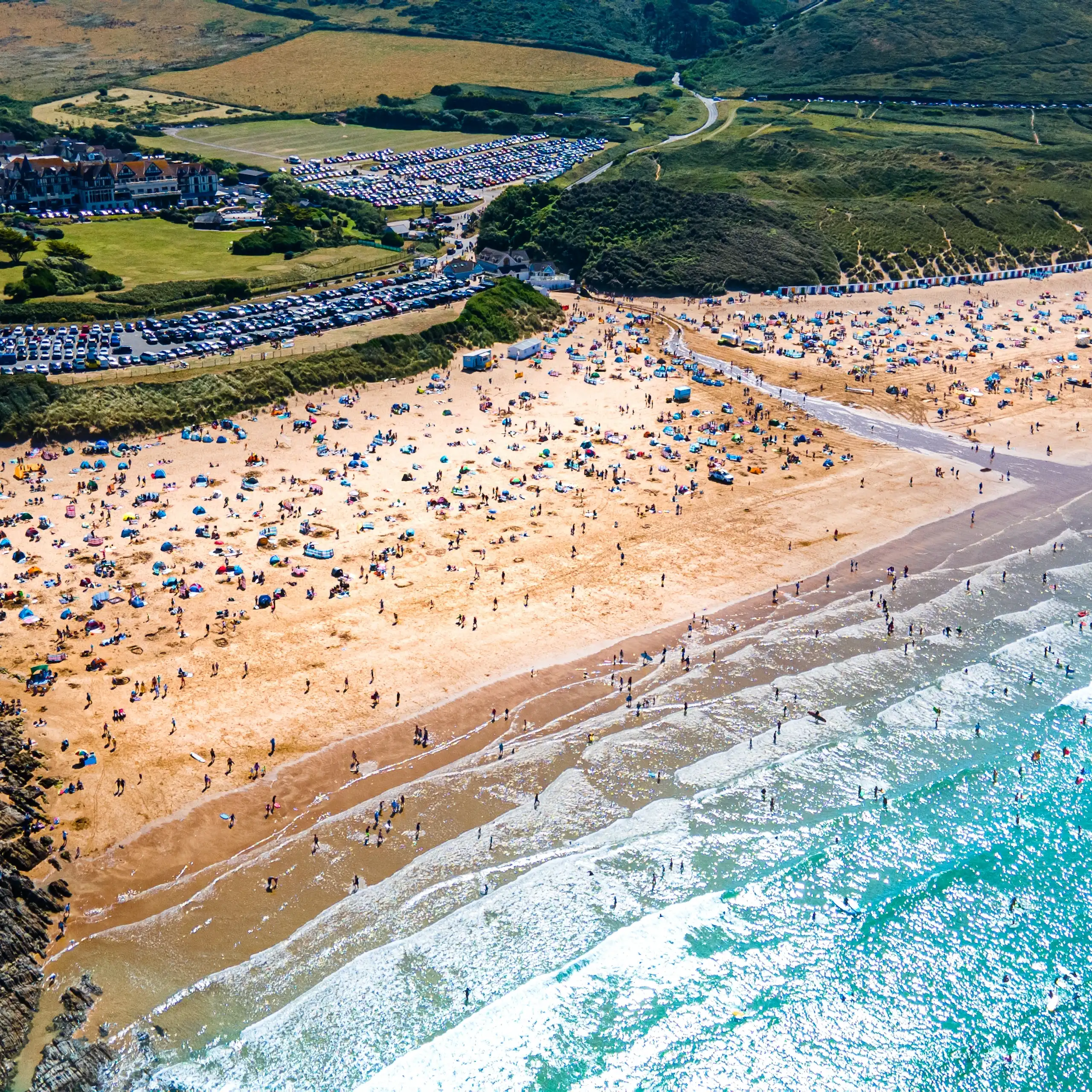 aerial shot of very busy beach, blue seas, hilly green coastline
