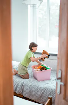 girl in bedroom tidying toys away into pink box