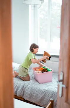 girl in bedroom tidying toys away into pink box