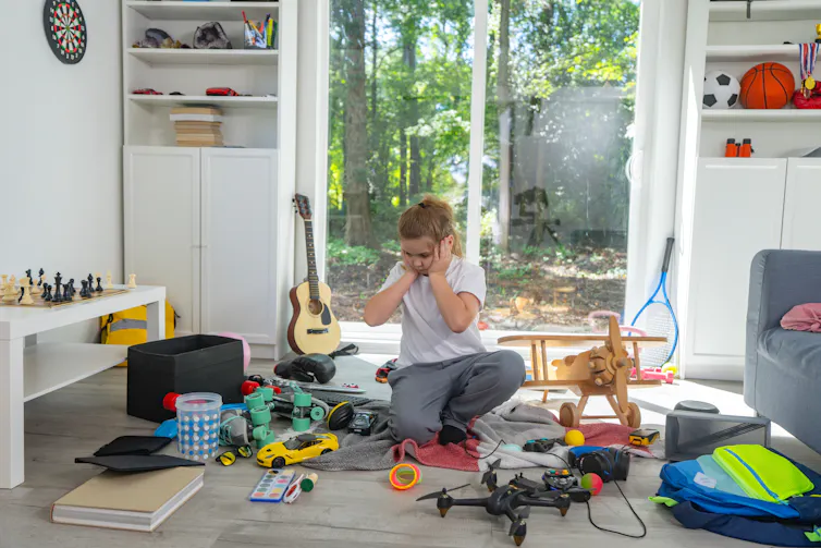 Child sat on bedroom floor, surrounded by messy toys
