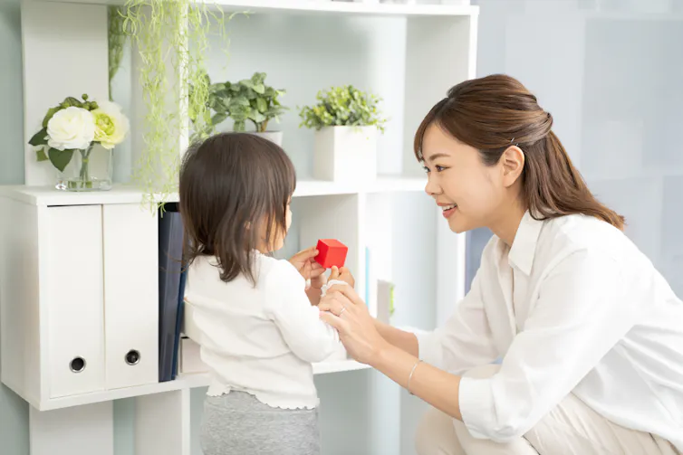 mum and daughter in white clothes in tody living room, putting one small red toy away