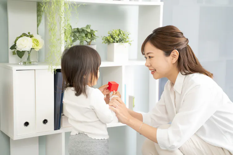 mum and daughter in white clothes in tody living room, putting one small red toy away