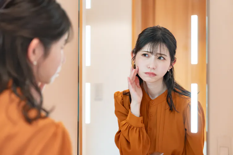 Woman looking in the mirror with a dissatisfied expression.