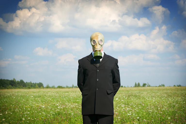 Un homme en costume avec un masque à gaz attend dans un champ.