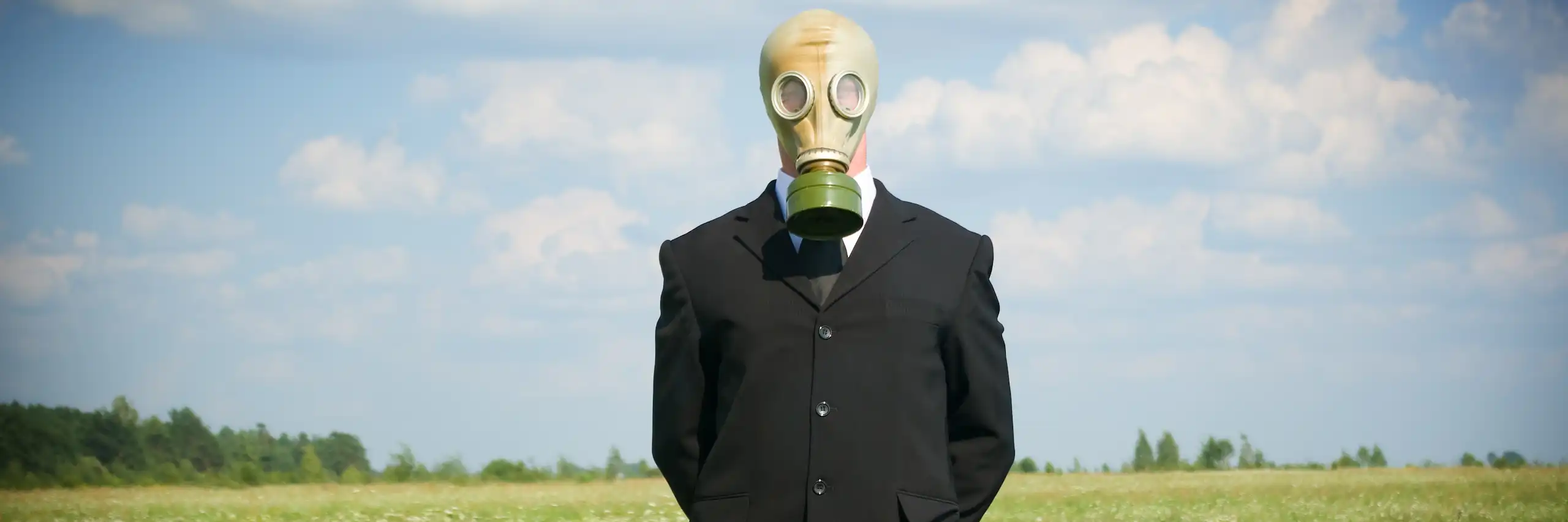 Un homme en costume avec un masque à gaz attend dans un champ.