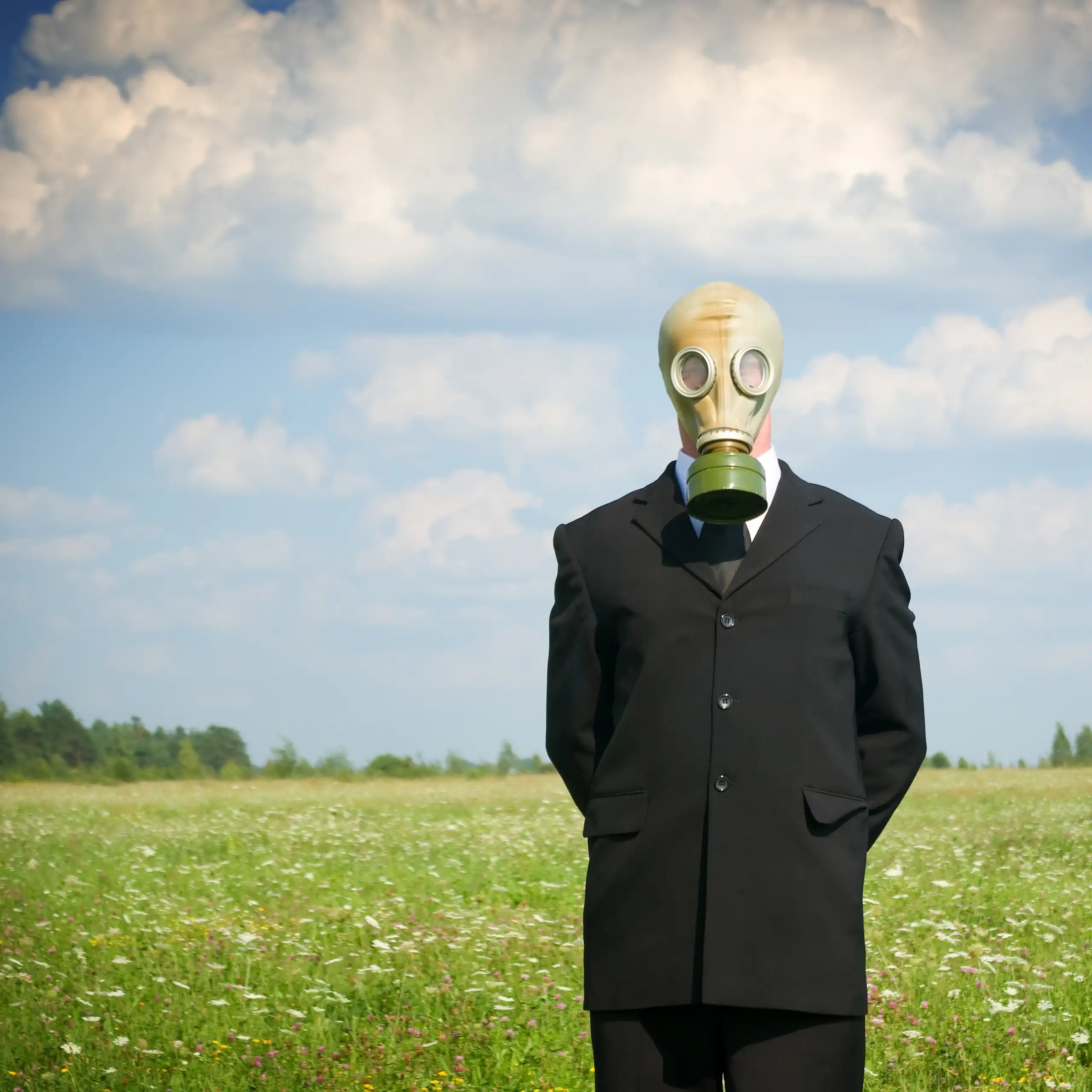 Un homme en costume avec un masque à gaz attend dans un champ.
