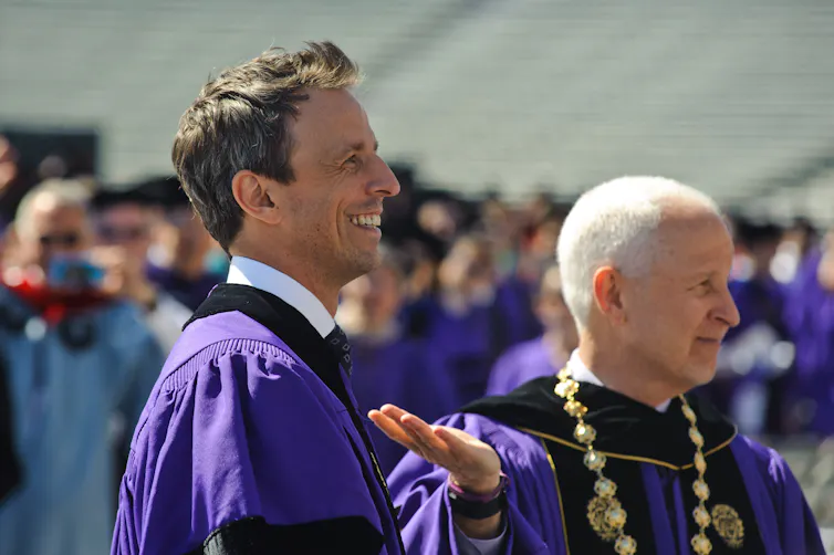 Two men wear purple robes and smile in a crowd of people.