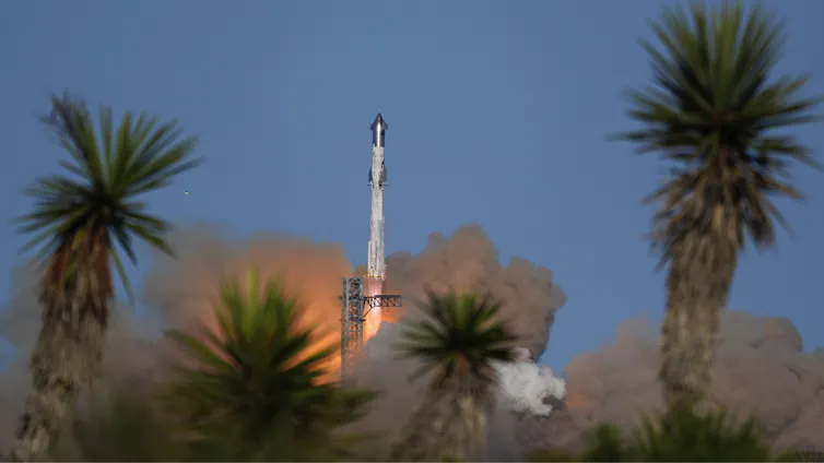 A rocket launching, with a plume of smoke and flame coming from below it and palm trees nearby.