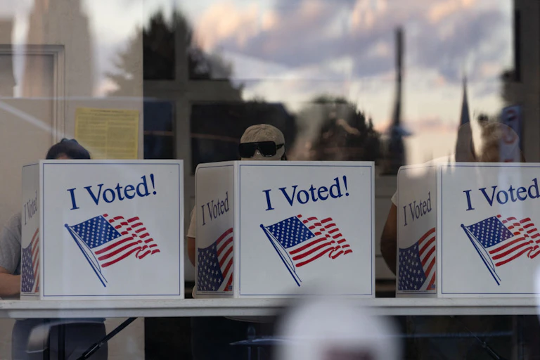 Three large white partitions read 'I Voted!' with voters behind it.