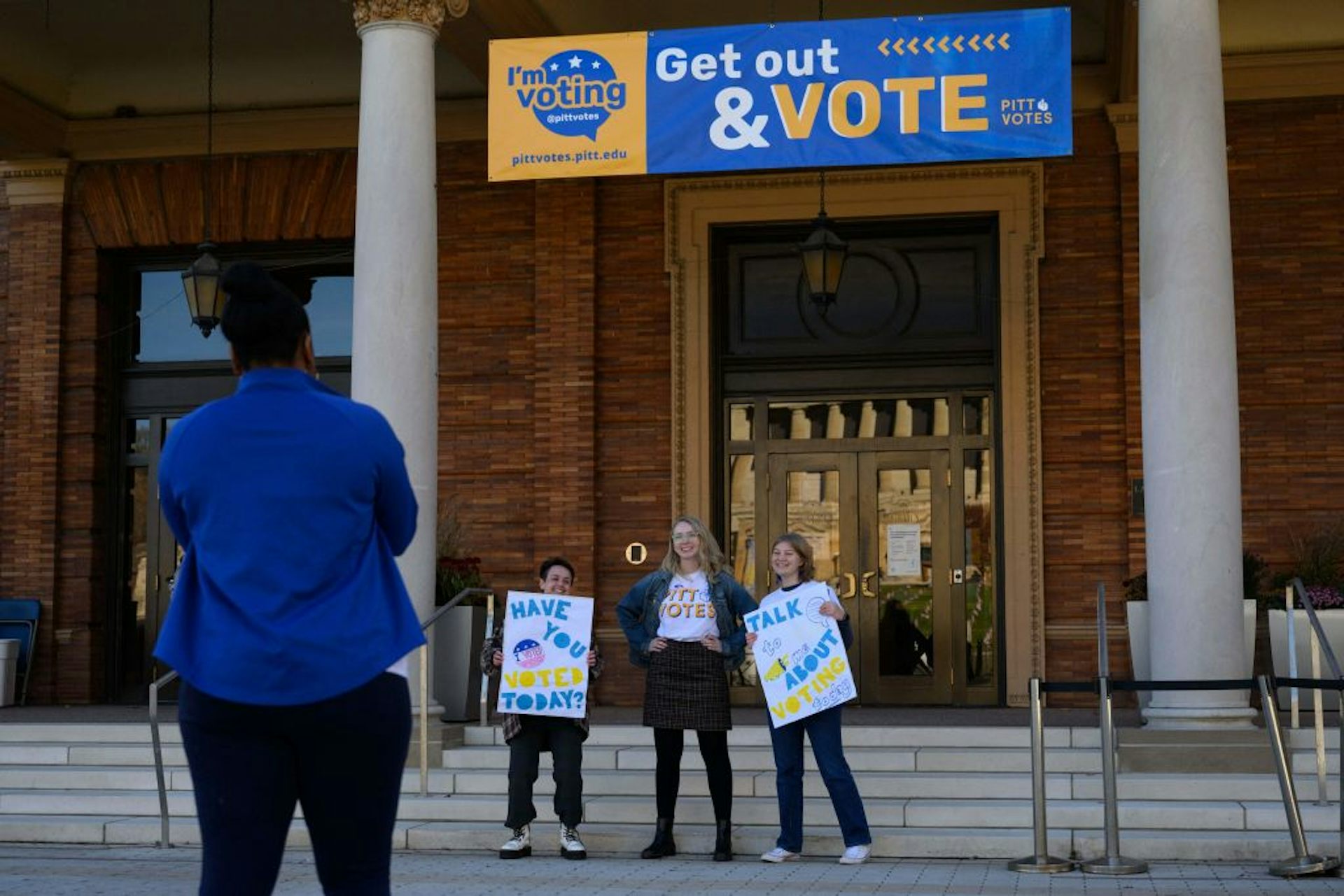 Tres mujeres jóvenes sostienen carteles de votación mientras están afuera.