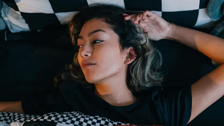 Woman lying in bed, looking out of window with a dismayed look on her face.