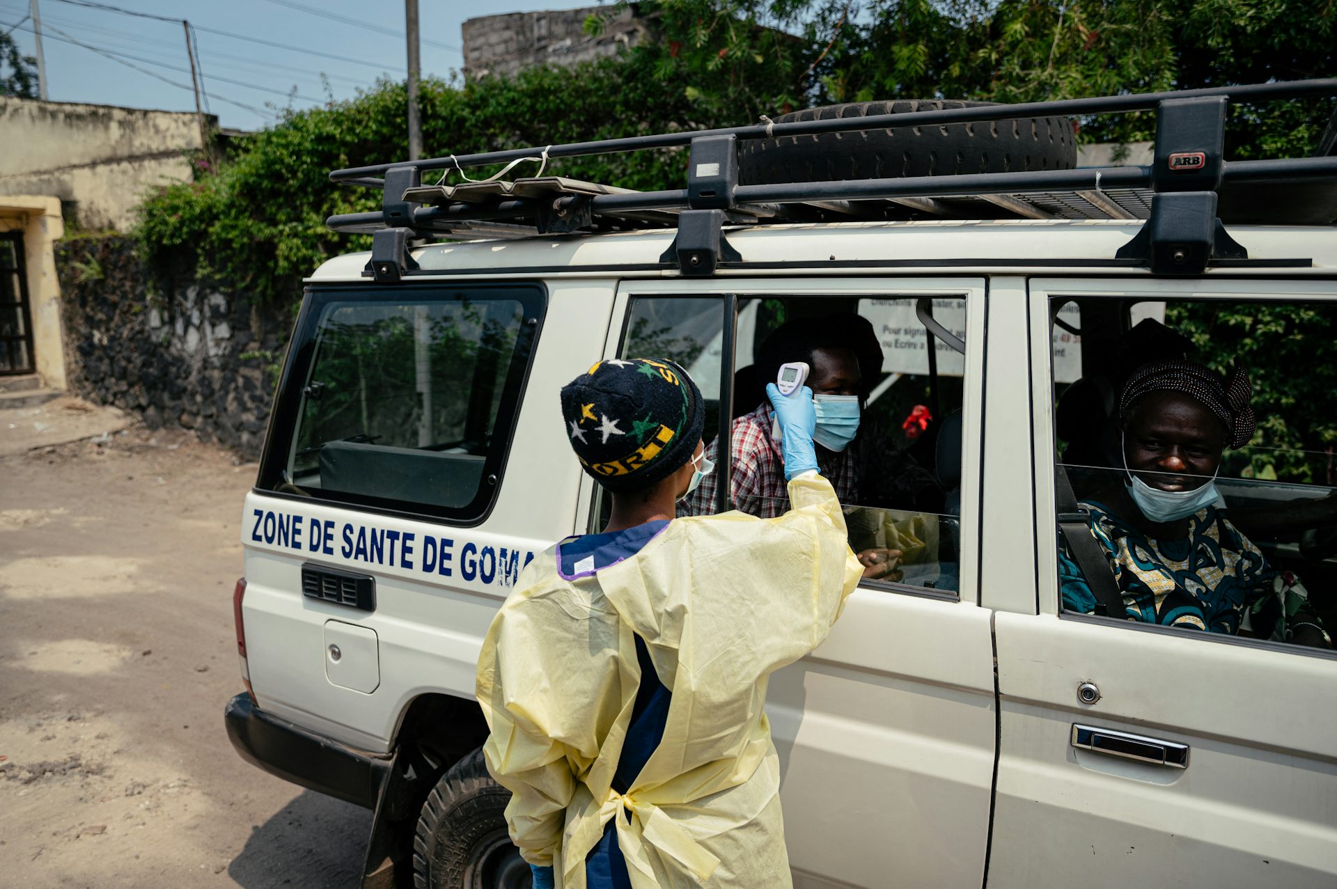 A person in protective gear checks the temperature of people in a white van.