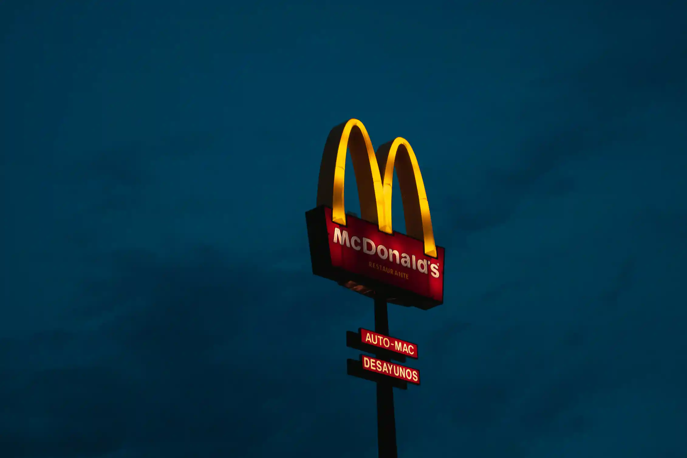 A lit-up McDonalds drive through sign against a night sky.