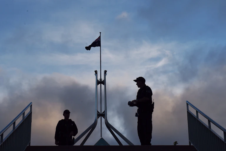 The shadowed outlines of two police officers in front of the Parliament House flag in Canberra.