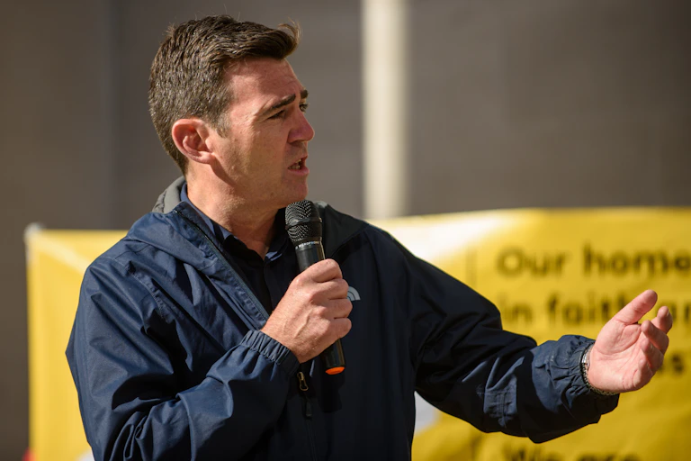 andy burnham with a microphone in hand addressing an audience