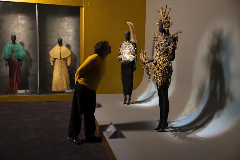 A gallery visitor examines sculptural dresses in an exhibition room.
