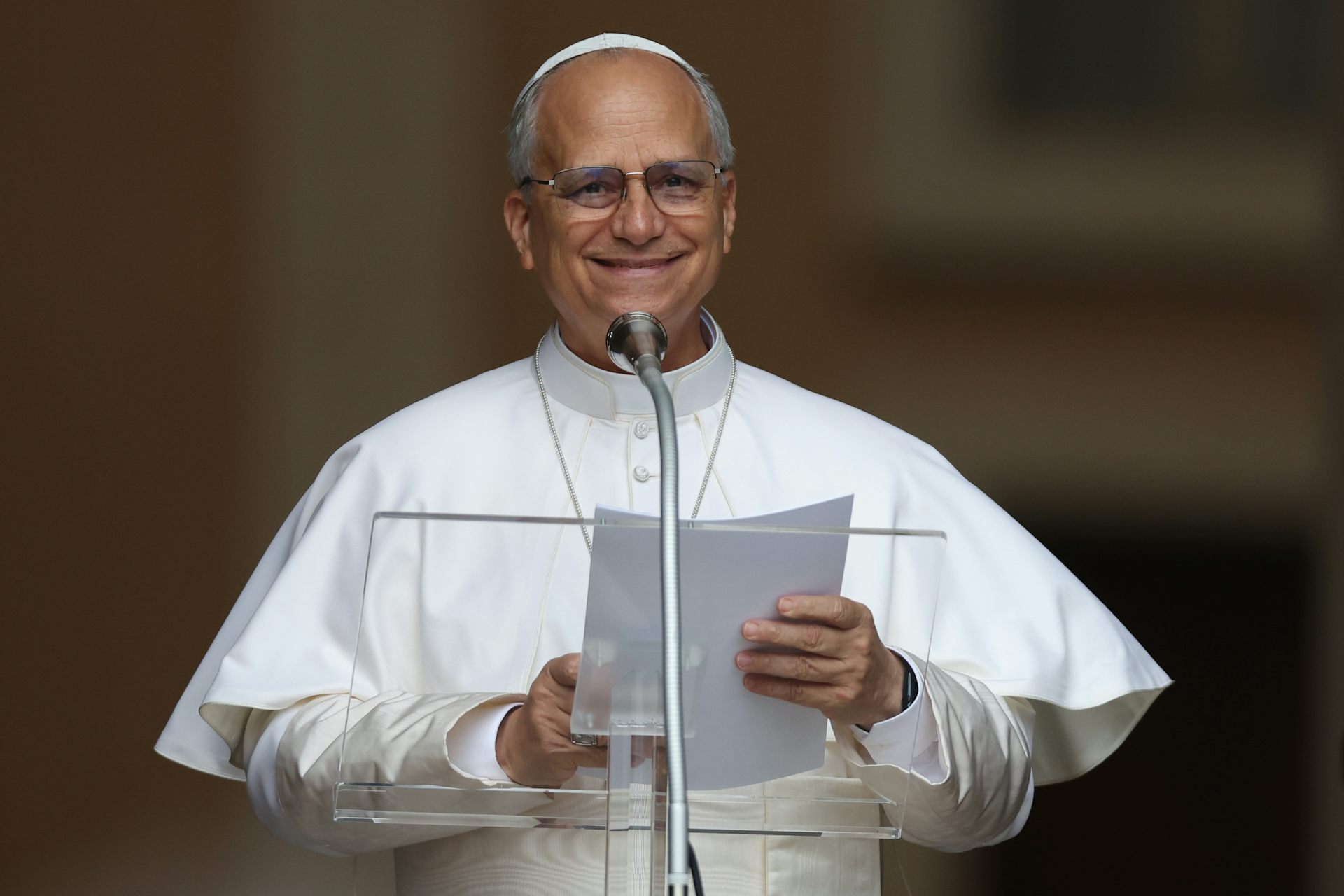 Un hombre sonriente vestido de blanco frente a un micrófono