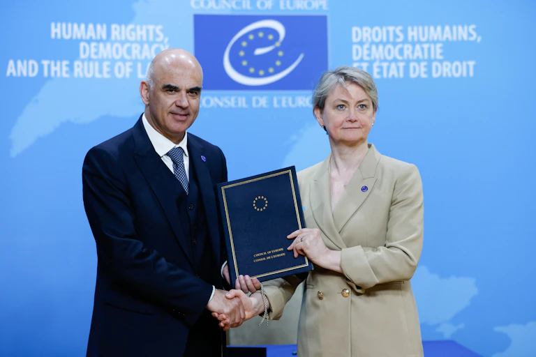 Cooper and Berset shaking hands while holding a blue folder