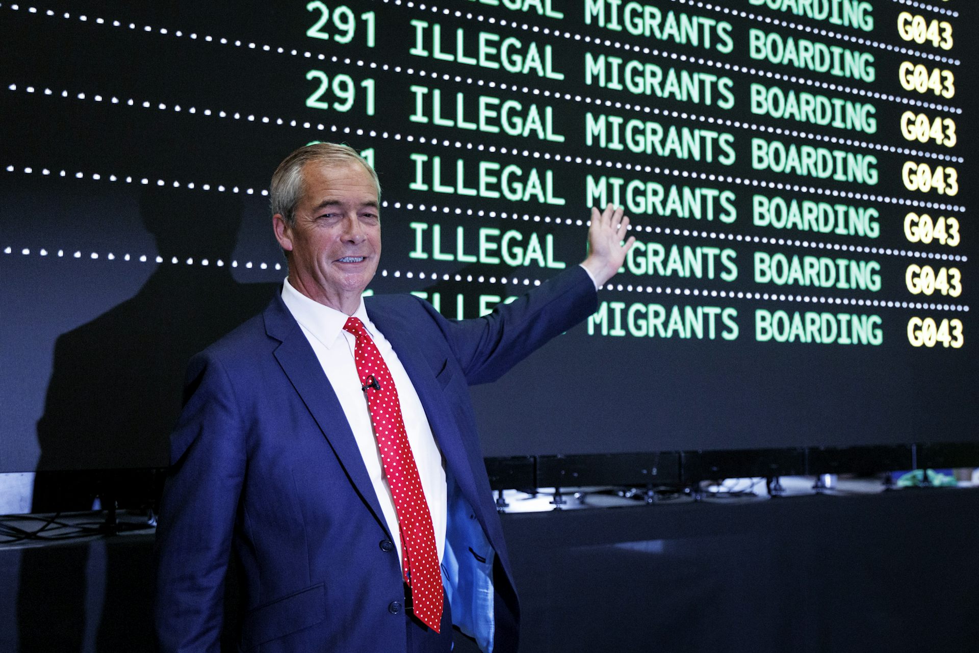 Nigel Farage in front of a mock departures board reading 'illegal migrants boarding'