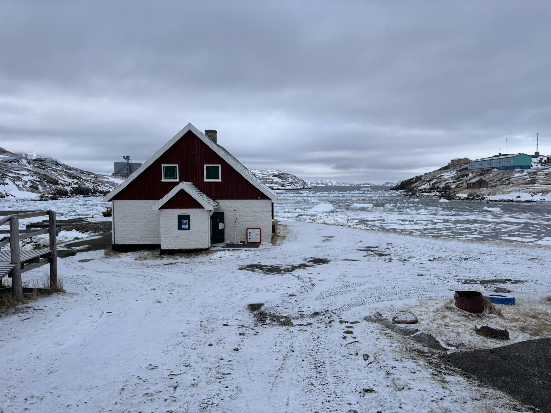 The Narsaq Museum on by snowed ground with icebergs floating in the surrounding Greenland Sea.