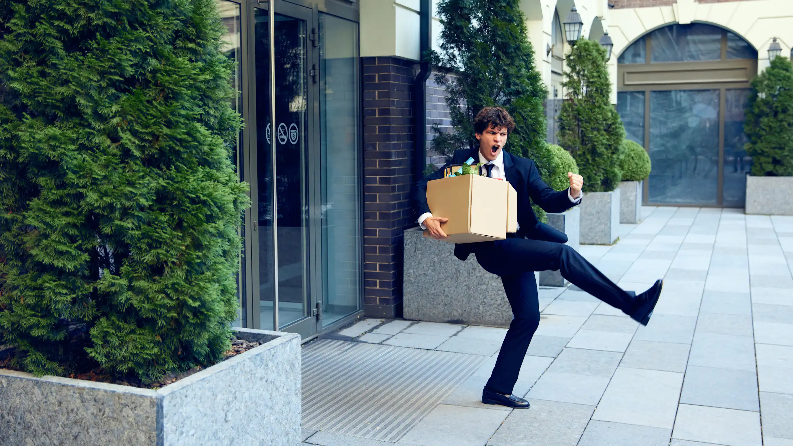 Personnage qui exulte en sortant d'un immeuble de bureaux avec son carton d'affaires personnelles.
