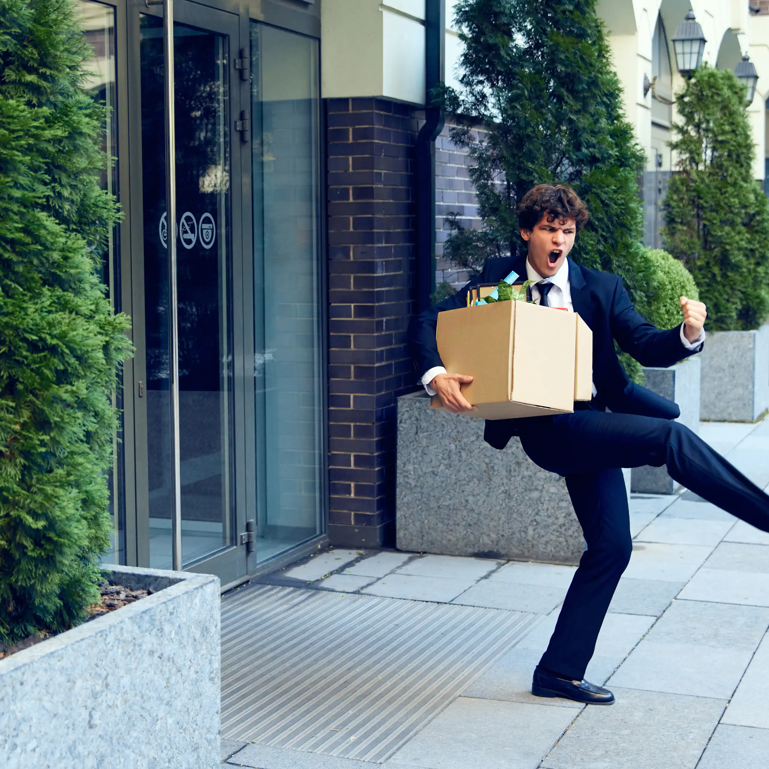Personnage qui exulte en sortant d'un immeuble de bureaux avec son carton d'affaires personnelles.