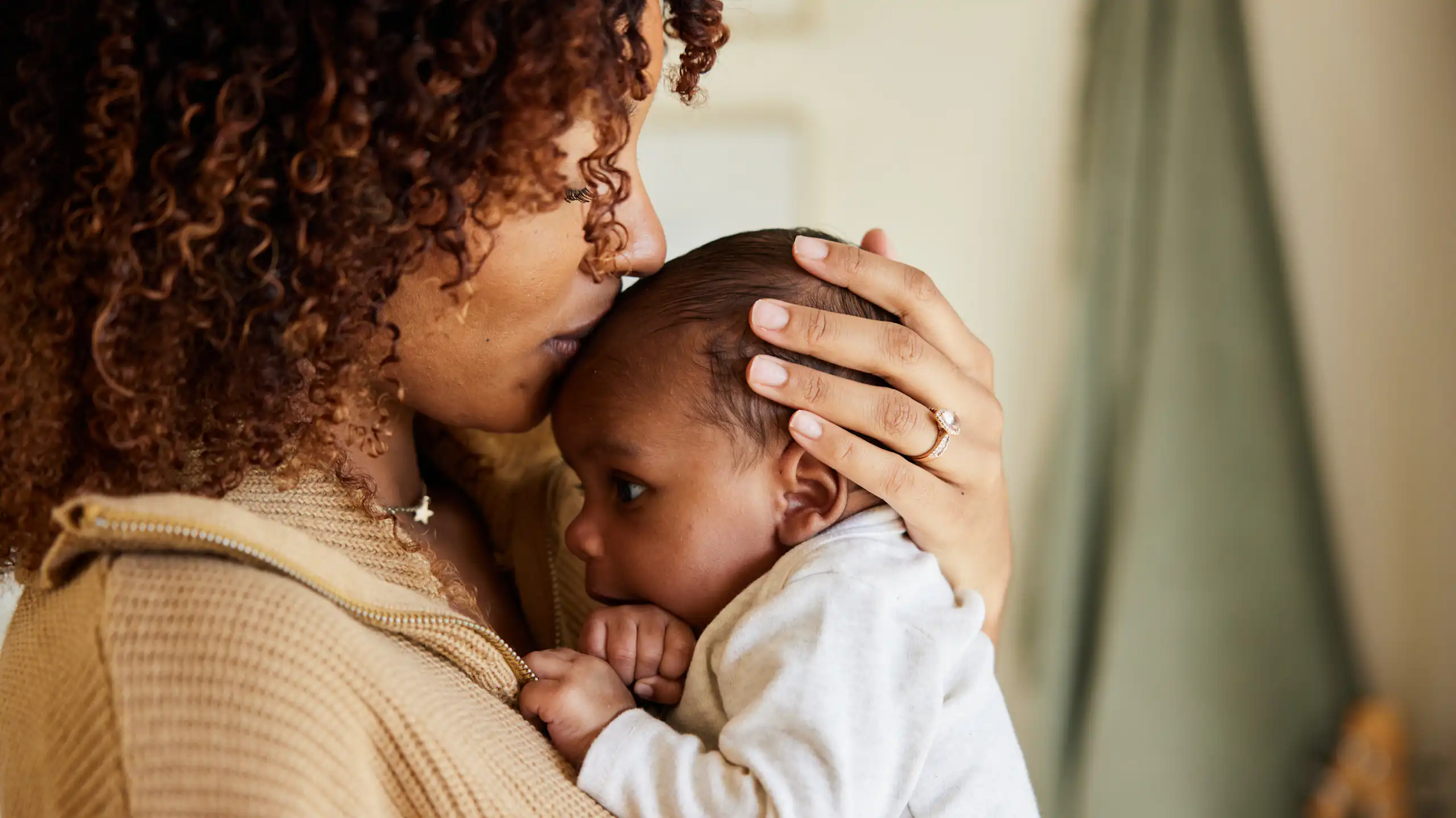 A Black mother kisses her newborn on its head.