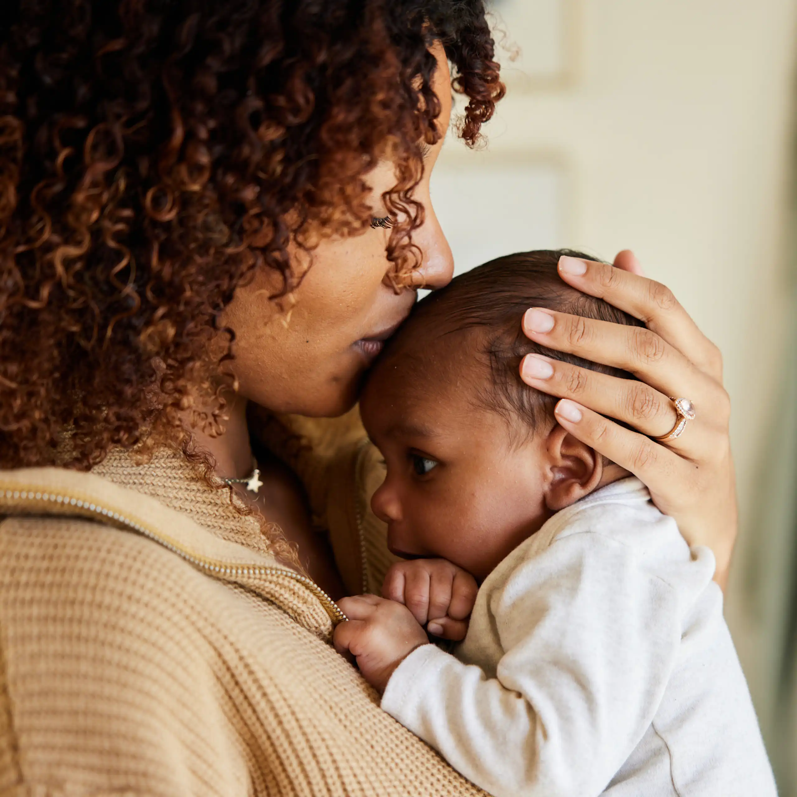 A Black mother kisses her newborn on its head.