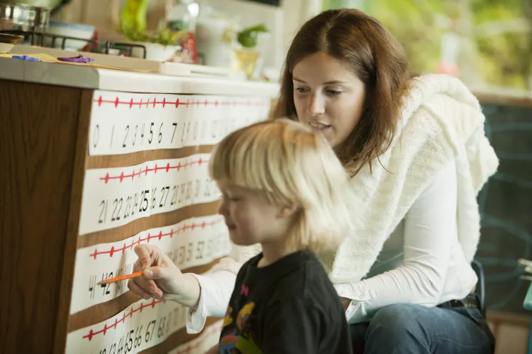 Woman kneeling next to young child points to number on a number line