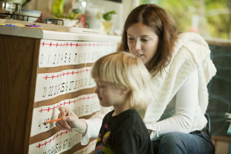 Woman kneeling next to young child points to number on a number line