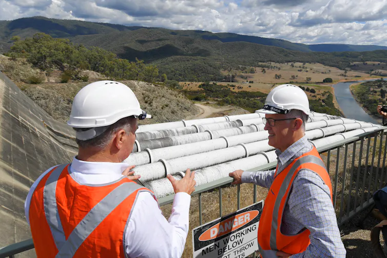 Two men standing in high vis gear and helmets with pipes in the background