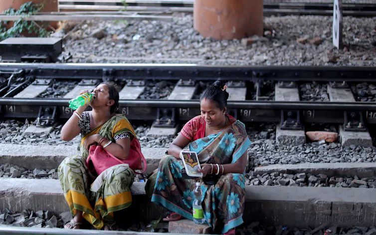 Two women sit on a train track, one of them drinking water.