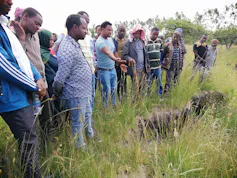 About 20 farmers stand next to a knee deep crack in the land