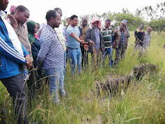 About 20 farmers stand next to a knee deep crack in the land