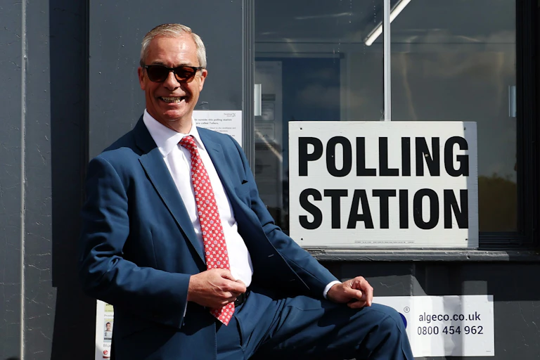 nigel farage in a dark suit and sunglasses appearing to dance in front of a polling station sign.
